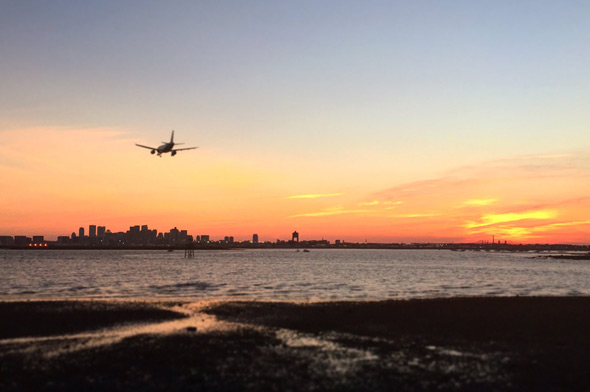Plane landing at Logan Airport at sunset over Boston Harbor