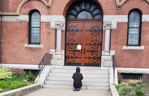 Woman praying outside closed church in Dorchester