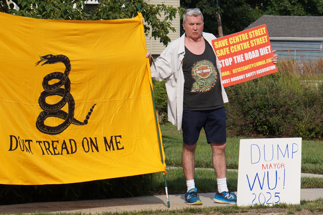 Man with a sign against the Centre Street road diet and Michelle Wu and a Don't Tread on Me flag