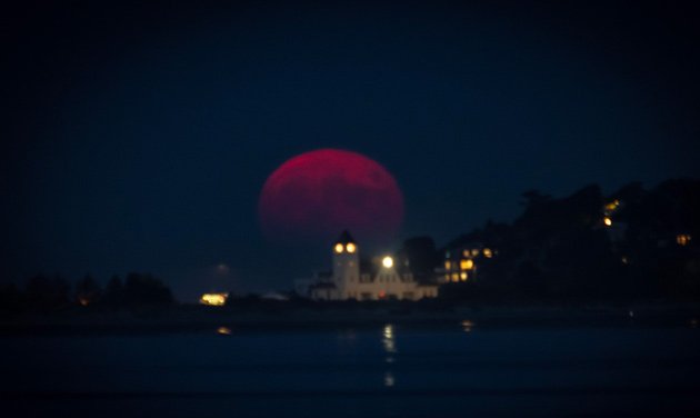 Blood-red hunter's moon rising over the water