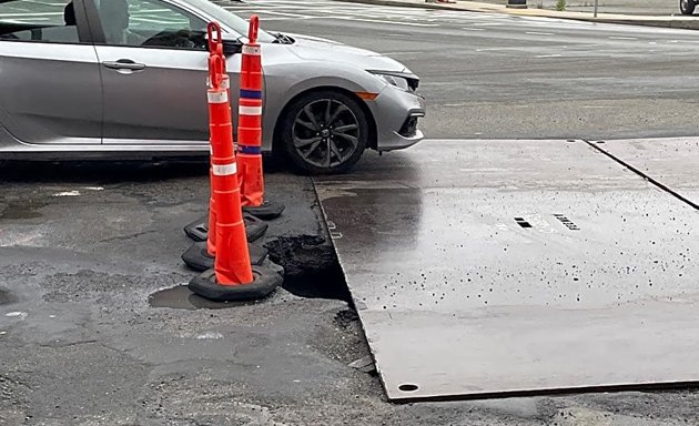 Large roadway hole covered by metal plate and traffic cones