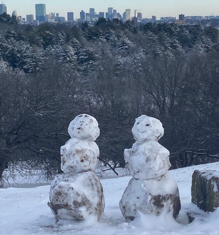 Snowmen at the top of Peters Hill in the Arboretum with downtown Boston and the Back Bay behind them