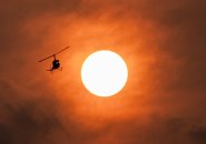 Helicopter flying through orange sky at sunset caused by Canadian wildfires